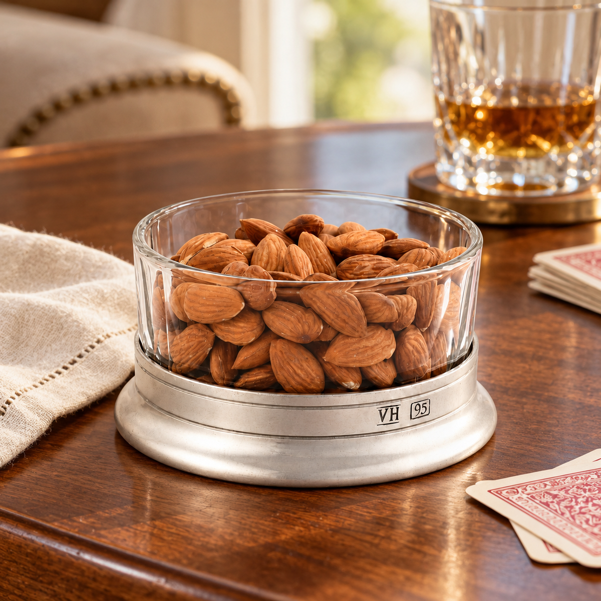 Glass and pewter bowl filled with almonds beside playing cards.